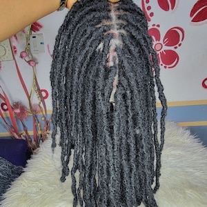 May include: Dark gray dreadlocks wig, featuring a natural-looking part. The dreadlocks are long and textured, with a slightly faded appearance. The wig is held up, showcasing the full length and style. A stylish hair accessory.