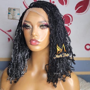 May include: A black and gray micro-loc wig on a mannequin head. The wig features a lace front and a natural-looking hairline. The mannequin has makeup and the Merit Hair logo is visible.