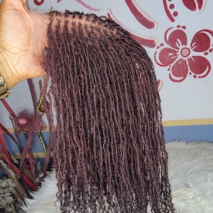 Könnte beinhalten: Burgunderfarbene Mikrolocks, eine Frisur mit zahlreichen kleinen, einzelnen Dreadlocks. Die Locs sind eng gewickelt und hängen herunter, wodurch ein strukturiertes Aussehen entsteht. Die Basis der Locs ist sichtbar, was zeigt, wie sie befestigt sind. Der Gesamtstil ist ein tiefes, sattes Burgunderrot.