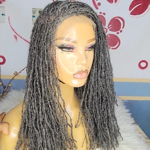 May include: A mannequin head displaying a gray dreadlock wig. The wig features a natural-looking hairline and is styled with numerous small, individual dreadlocks. The mannequin is set against a backdrop with floral and abstract patterns.