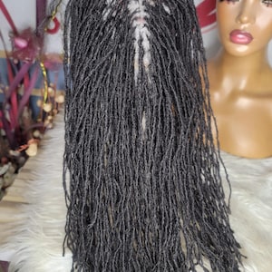 May include: A dark gray wig with long, thin dreadlocks. The wig is held up, showcasing the intricate parting and the texture of the individual dreads. A mannequin head is visible in the background.