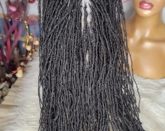 Può includere: Una parrucca grigio scuro con lunghe e sottili trecce rasta. La parrucca è tenuta in mano, mostrando l'intricata separazione e la consistenza delle singole trecce. Sullo sfondo è visibile una testa di manichino.
