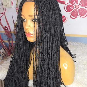 Könnte beinhalten: Schwarze Dreadlock-Perücke auf einem Schaufensterkopf. Die Perücke hat lange, einzelne Dreadlocks, die um die Schultern fallen. Der Schaufensterkopf hat einen hellen Hautton, und der Hintergrund ist eine Wand mit floralen Mustern.