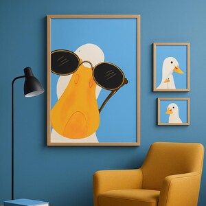May include: A set of framed art prints featuring a cartoon duck wearing sunglasses. The main print shows a close-up of the duck's face, with two smaller prints of the duck's head. The prints are displayed on a blue wall.