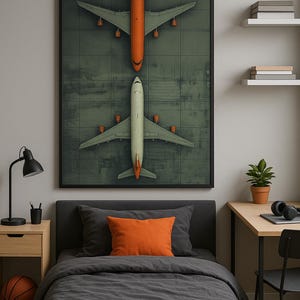 Puede incluir: Una impresi&oacute;n enmarcada que representa dos aviones, uno naranja y otro blanco, sobre un fondo verde. La obra de arte se exhibe sobre una cama con ropa de cama gris y una almohada naranja. Tambi&eacute;n se ve una pelota de baloncesto y una l&aacute;mpara de escritorio.