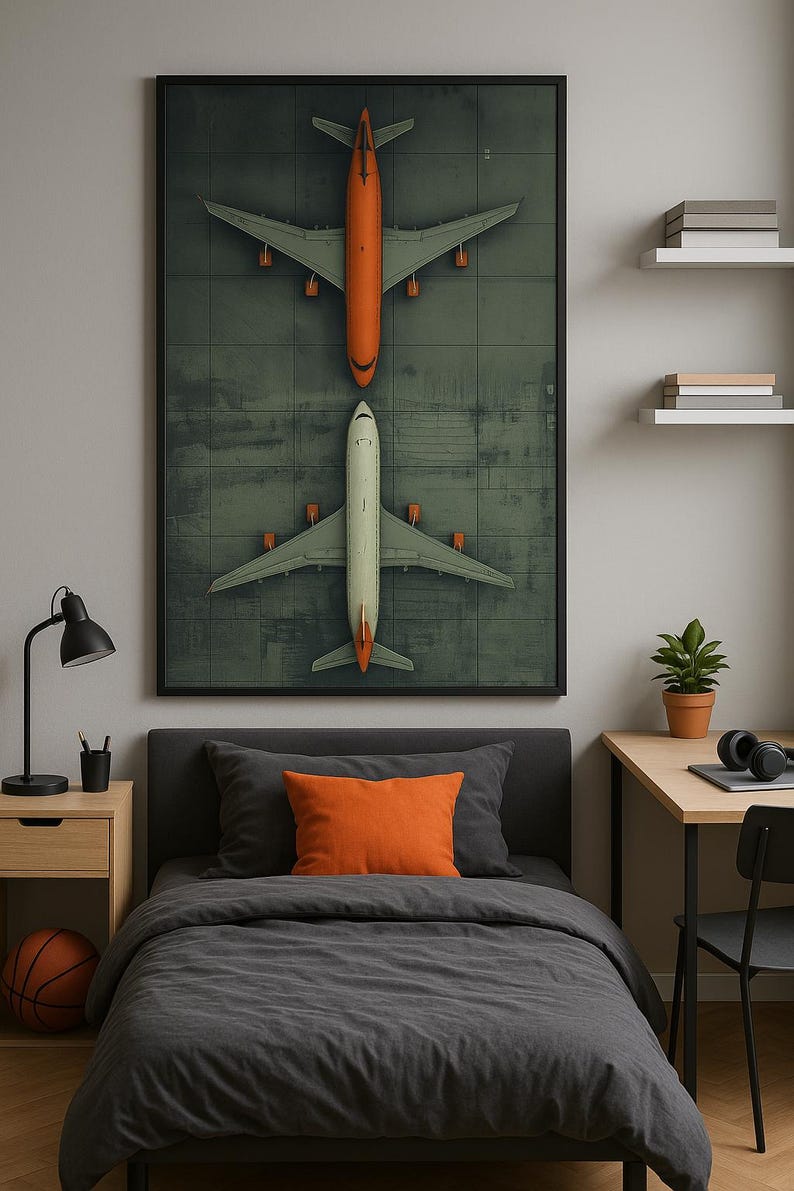 Puede incluir: Una impresi&oacute;n enmarcada que representa dos aviones, uno naranja y otro blanco, sobre un fondo verde. La obra de arte se exhibe sobre una cama con ropa de cama gris y una almohada naranja. Tambi&eacute;n se ve una pelota de baloncesto y una l&aacute;mpara de escritorio.