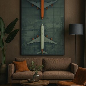 Puede incluir: Una obra de arte enmarcada con dos vistas a&eacute;reas de aviones en una pista verde y gris. El avi&oacute;n superior es naranja y el inferior es blanco. La obra cuelga sobre un sof&aacute; marr&oacute;n con un coj&iacute;n naranja.