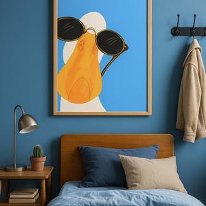 May include: A framed art print featuring a cartoon duck wearing sunglasses against a blue background. The duck has an orange beak and is set in a light wood frame. The image is hanging above a bed with blue bedding and pillows.