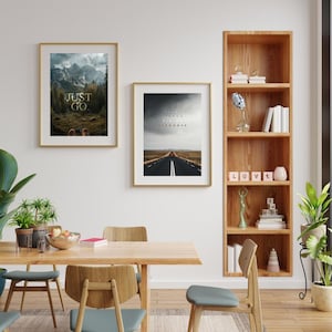 K&ouml;nnte beinhalten: Zwei gerahmte Kunstdrucke mit goldenen Rahmen an einer wei&szlig;en Wand. Einer zeigt eine Berglandschaft mit dem Text "JUST GO". Der andere zeigt eine Stra&szlig;e zum Horizont mit dem Text "STOP FEELING START DOING FEEL STRONGER."