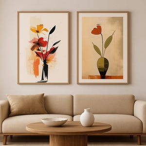 May include: Two framed abstract floral art prints. One features yellow and red flowers in a black vase, the other a single red flower in a green vase. The prints are displayed above a beige sofa with a round wooden coffee table.