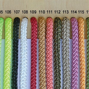 May include: A collection of 16 different coloured cords, numbered 103 to 118, displayed on a wooden surface. The cords are all the same length and are arranged in a row.