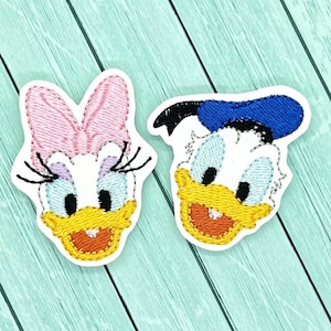 May include: Two embroidered cartoon character patches. The patch on the left is a pink and white duck with a pink bow. The patch on the right is a blue and white duck with a blue sailor hat.