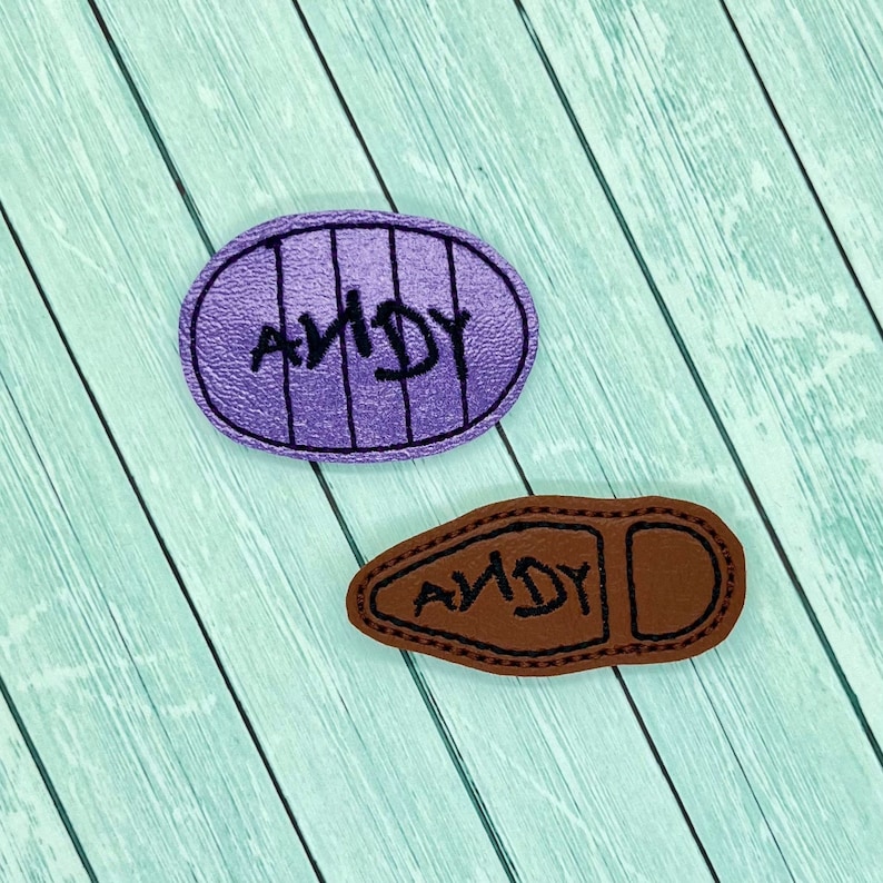 May include: Two purple and brown felt patches with the word "ANDY" embroidered on them. The patches are shaped like a shoe and a circle.