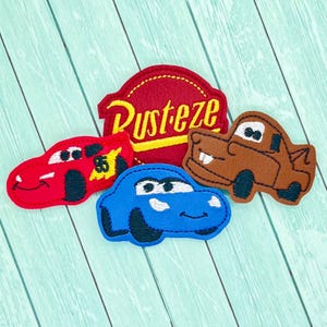 May include: Four felt appliques featuring characters from the Disney Pixar movie Cars. The appliques include Lightning McQueen, Mater, and a blue car. The fourth applique is a red circle with the words "Rust-eze" in yellow.