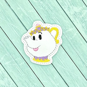May include: Embroidered patch of Mrs. Potts, a character from Disney's Beauty and the Beast. The patch is white with yellow, purple, and pink details. It features a teapot with a face and a crown.