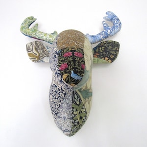 Op de afbeelding: Een patchwork hertenkop wanddecoratie gemaakt van stof met bloemen- en vogelpatronen in tinten blauw, groen, roze en bruin.