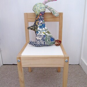 May include: A wooden chair with a white seat and a colourful patchwork bunny rabbit sitting on it.