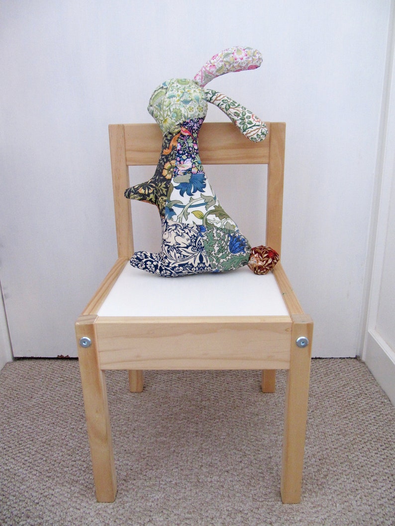 May include: A wooden chair with a white seat and a colourful patchwork bunny rabbit sitting on it.