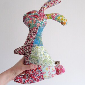 May include: A patchwork fabric bunny toy with a floral pattern. The bunny is made of different coloured fabrics, including pink, blue, green, and red. The bunny has a long, floppy ear and a small tail.