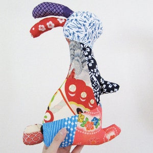 May include: A patchwork rabbit toy made from colourful fabric scraps. The rabbit has a long, floppy ear and a tail. The fabric is a mix of floral, geometric, and abstract patterns.
