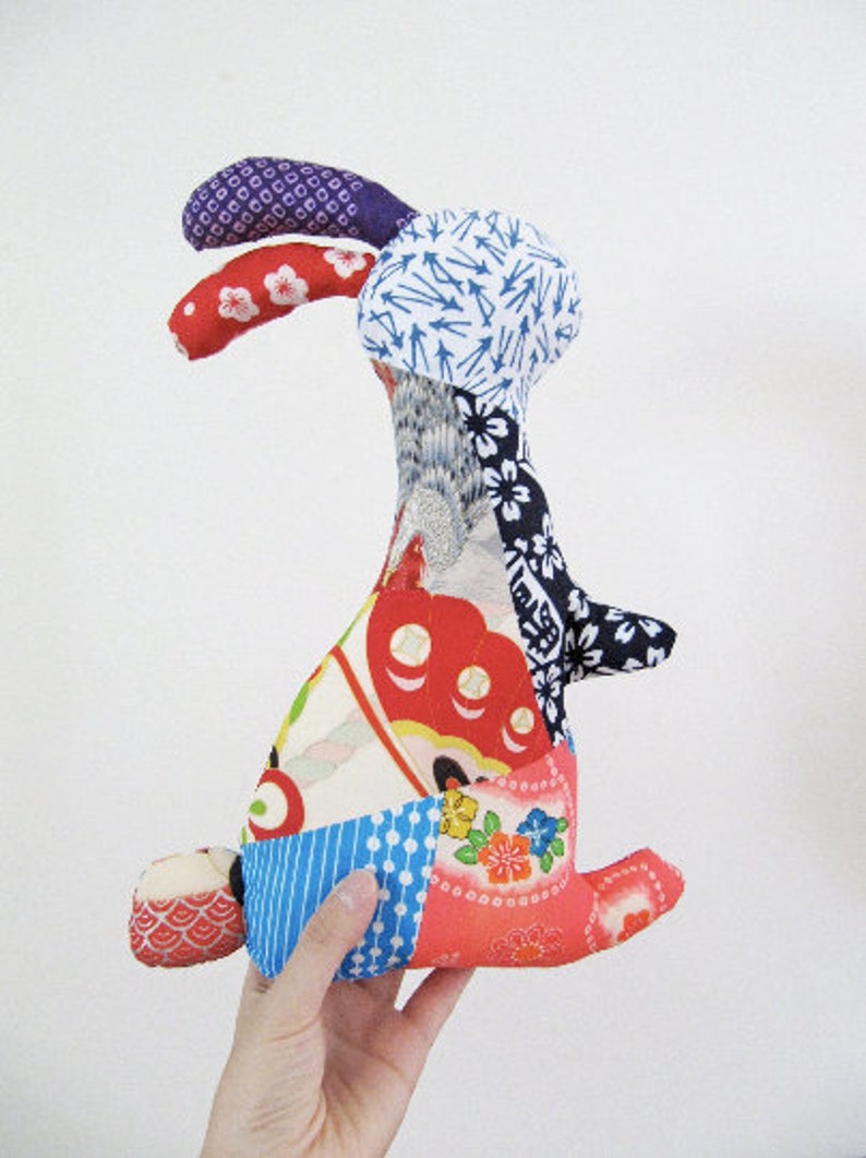 May include: A patchwork rabbit toy made from colourful fabric scraps. The rabbit has a long, floppy ear and a tail. The fabric is a mix of floral, geometric, and abstract patterns.