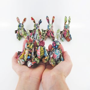 May include: A group of seven handmade fabric bunny rabbits in various floral patterns. The bunnies are sitting on a white surface.