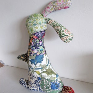 May include: A patchwork rabbit toy made from colourful floral fabric. The rabbit has long ears and a tail. The fabric is a mix of green, blue, white, and pink.