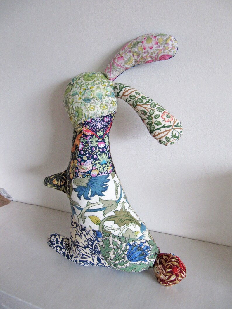 May include: A patchwork rabbit toy made from colourful floral fabric. The rabbit has long ears and a tail. The fabric is a mix of green, blue, white, and pink.