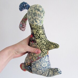 May include: A patchwork fabric bunny toy with a blue, green and yellow floral pattern. The bunny is made of different fabrics sewn together in a patchwork style.