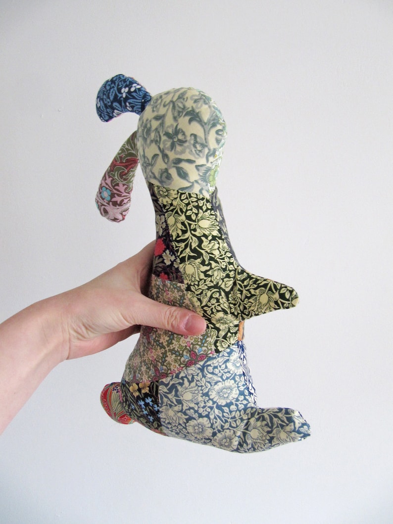 May include: A patchwork fabric bunny toy with a blue, green and yellow floral pattern. The bunny is made of different fabrics sewn together in a patchwork style.
