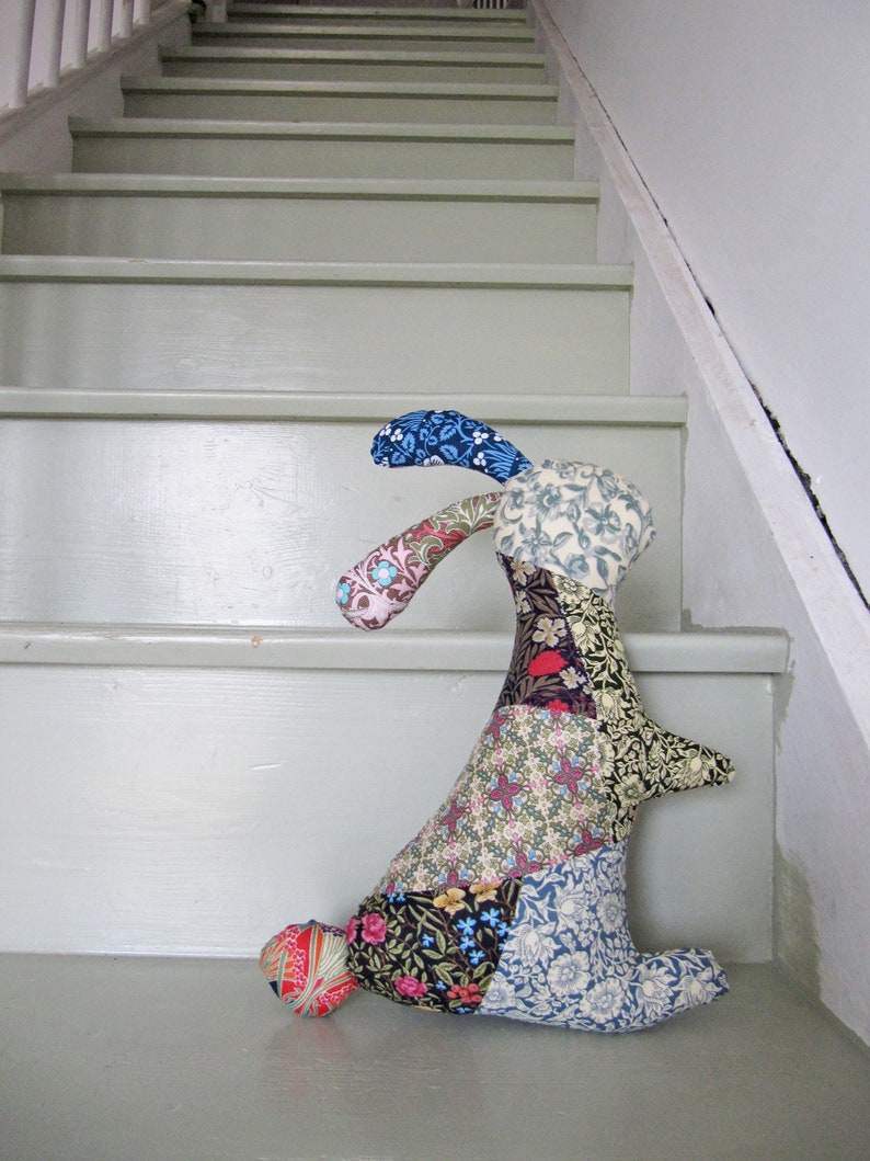 May include: A patchwork fabric bunny toy with blue, green, red and white floral patterns. The bunny is sitting on a set of white painted stairs.