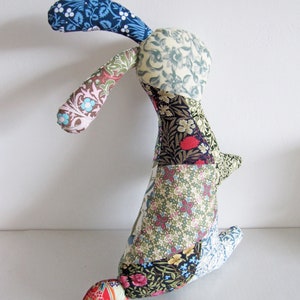 May include: A patchwork bunny toy with a long, floppy ear. The bunny is made from a variety of floral fabrics in shades of blue, green, red, and yellow.
