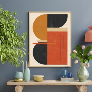 Könnte beinhalten: Ein gerahmter abstrakter Kunstdruck mit geometrischen Formen in Orange, Schwarz und Beige. Das Kunstwerk wird auf einem Holztisch mit dekorativen Vasen und einem kleinen Baum ausgestellt. Die Farbpalette umfasst Orangetöne, Schwarz, Beige und Blau.
