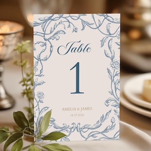 May include: A table number card with a floral design. The card features the word "Table" above the number "1" in a dark blue font. The names "Amelia & James" and the date "18.07.2026" are printed at the bottom.