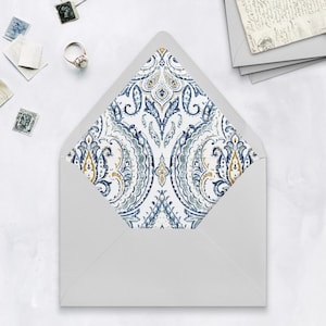 Puede incluir: Un sobre blanco con un interior estampado. El diseño interior presenta un diseño de cachemira azul, dorado y gris. El sobre está abierto, revelando el intrincado patrón. Sellos y un anillo están esparcidos alrededor del sobre.