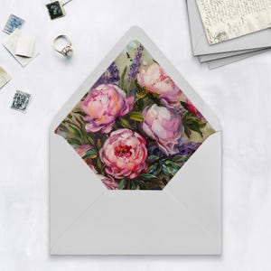 May include: A white envelope with a floral design. The interior features a painting of pink peonies and lavender. The envelope is open, revealing the artwork. Stamps and a ring are scattered around the envelope on a white surface.
