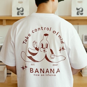 May include: White t-shirt with a brown graphic of a banana with a face and the text "Take control of mid EST. 2001 ++ BANANA now on inferno"