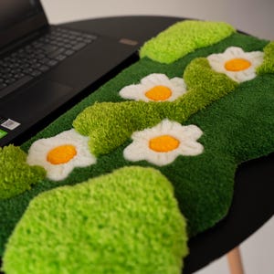 May include: A tufted rug featuring a vibrant green background with textured lime green patches and three white daisy flowers with bright yellow centers. The rug has a soft, plush pile and an irregular, organic shape with rounded edges.