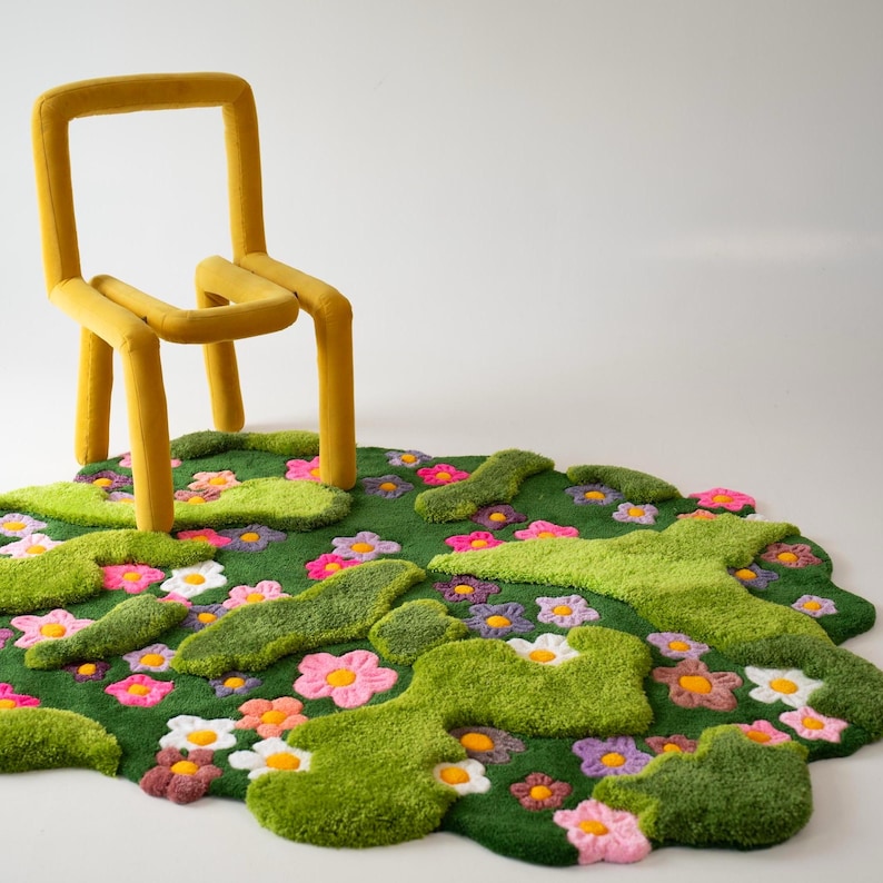 May include: A mustard yellow chair with a rounded, tubular frame positioned next to an irregular, tufted rug featuring a deep green base with raised light green patches and a variety of small, colorful flowers in pink, white, and orange.