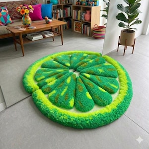 Puede incluir: Una alfombra circular con mechones en forma de rodaja de lima, con una corteza verde vibrante y secciones interiores segmentadas en varios tonos de verde lima y verde amarillento, con una superficie texturizada y afelpada que imita la fruta.