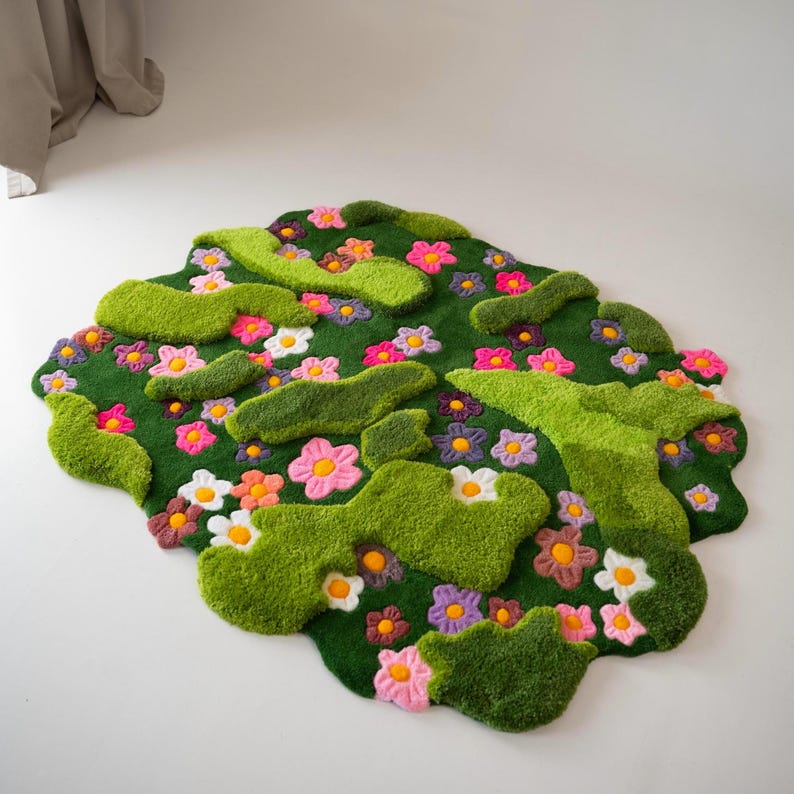 May include: A tufted rug with an irregular, organic shape featuring a deep green base. The surface is decorated with various small, multi-colored flowers in shades of pink, purple, orange, and white, interspersed with raised, textured lime green patches.
