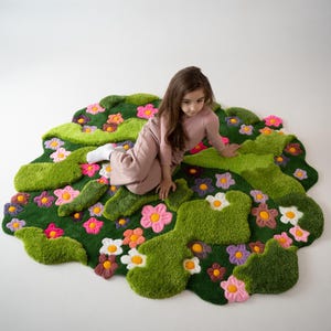 May include: A tufted area rug with an irregular, organic shape featuring a deep green base, raised light green moss-like patches, and various small flowers in shades of pink, purple, white, and orange with yellow centers scattered throughout.