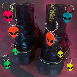 May include: A pair of black leather boots with yellow straps and alien-shaped keychains. The keychains are in various colors, including pink, green, orange, and yellow.