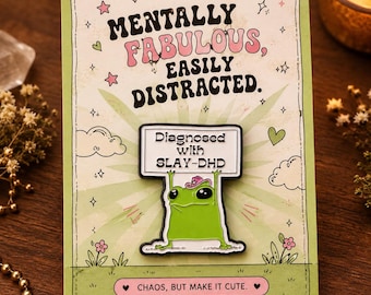 May include: A green enamel pin featuring a frog wearing a pink cowboy hat and holding a sign that reads Diagnosed with SLAY-DHD. The pin is attached to a light green backing card with the text Mentally Fabulous, Easily Distracted and Chaos, but make it cute.