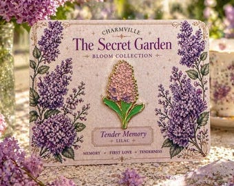 May include: A lilac flower pin from the Bloom Collection, Tender Memory. The pin is a light pink and purple flower with green leaves, set against a cream-colored background. The card reads "The Secret Garden" and "Charmville".