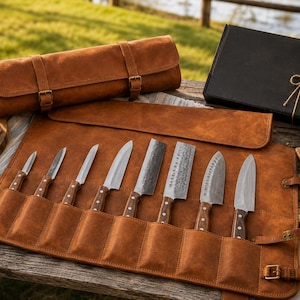 Könnte beinhalten: Eine braune Messertasche aus Leder mit acht Küchenmessern mit Holzgriffen. Das Set enthält verschiedene Klingenformen, darunter Schäl-, Universal- und Hackmesser. Die Tasche ist mit verstellbaren Schnallenriemen versehen und offen ausgelegt.