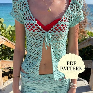 May include: A light mint green crochet set consisting of a short-sleeved, open-front cardigan with a tie closure and matching fitted shorts. A cream-colored shell-shaped graphic with the black text PDF PATTERN is overlaid on the image.
