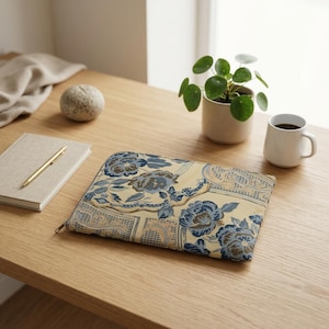May include: A rectangular zippered pouch featuring a woven floral pattern in shades of blue, cream, and tan. The fabric displays a detailed design of large blossoms and geometric grid motifs across the entire surface of the flat accessory case.