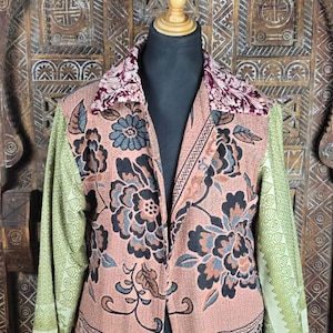 Könnte beinhalten: Eine langärmelige Jacke mit pfirsichfarbener Basis und dunklem Blumenmuster, hellgrün gemusterten Ärmeln und einem dunkelvioletten Samtkragen. Das Kleidungsstück hat einen geraden Saum, der mit einer Fransenborte abgeschlossen ist.