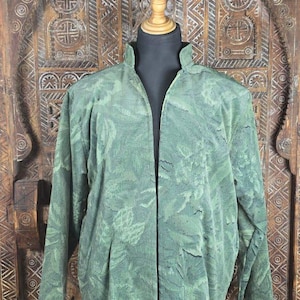 Könnte beinhalten: Eine langärmelige, vorne offene Jacke in Salbei- und Waldgrüntönen mit einem durchgehenden, tonalen Jacquard-Blumenmuster. Das Kleidungsstück verfügt über einen Stehkragen, einen geraden Saum und eine strukturierte Stoffoberfläche auf einer Schneiderpuppe.